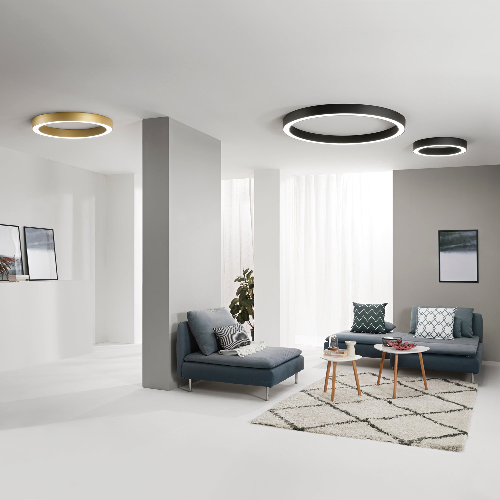 Plafoniere LED moderne a forma circolare con luce diffusa, disponibili in finitura oro e nero, installate su soffitto in un soggiorno contemporaneo con divano, tavolino e arredamento minimal.
